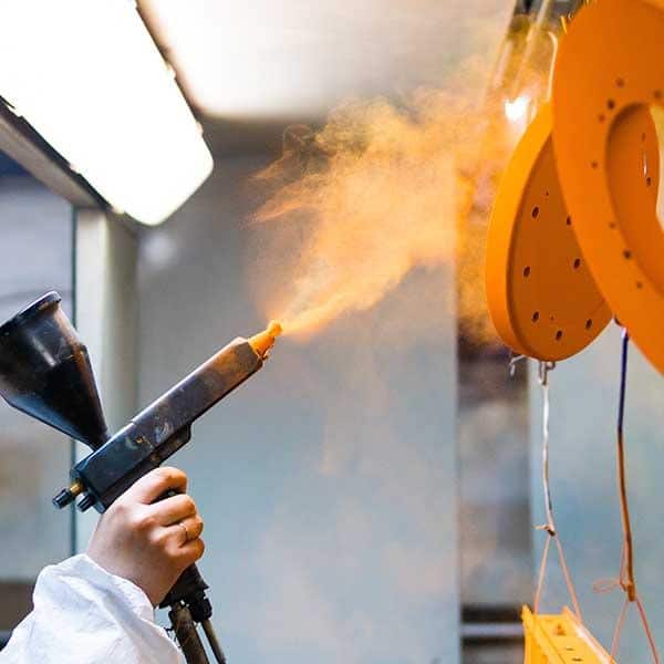 Powder coating of metal parts. A woman in a protective suit sprays powder paint from a gun on metal products orange powder coating of metal parts with spray gun