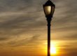 LED acrylic globe with large cap and arms post top luminaire with finial overlooking river at sunset