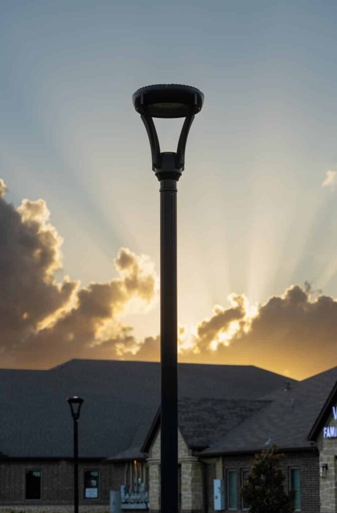 Two modern lamp post, H-01 Series, in front of a setting sun and a TruVet Hospital.