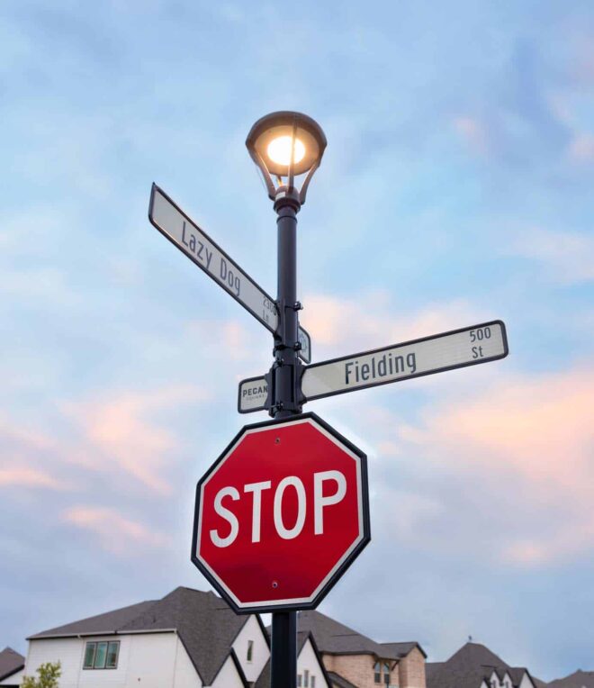 H-01 Series post top luminaire with street signs and a stop sign in a residential area.