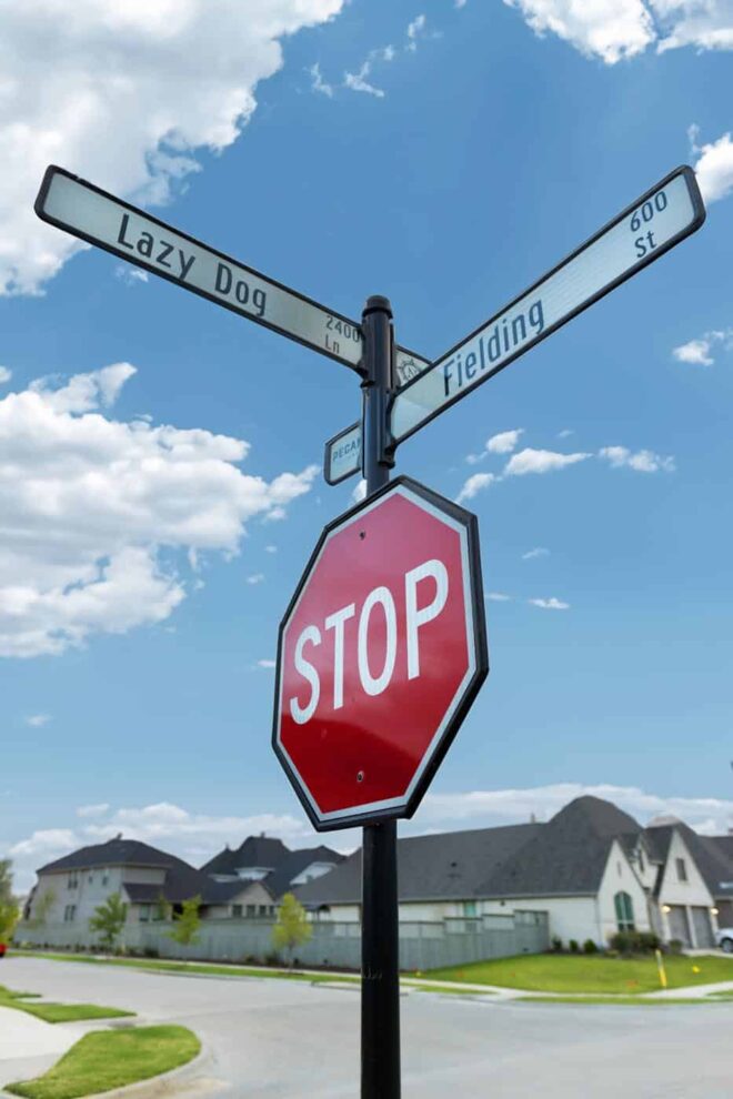 Street sign with a round pole and a decorative finial in a residential intersection.