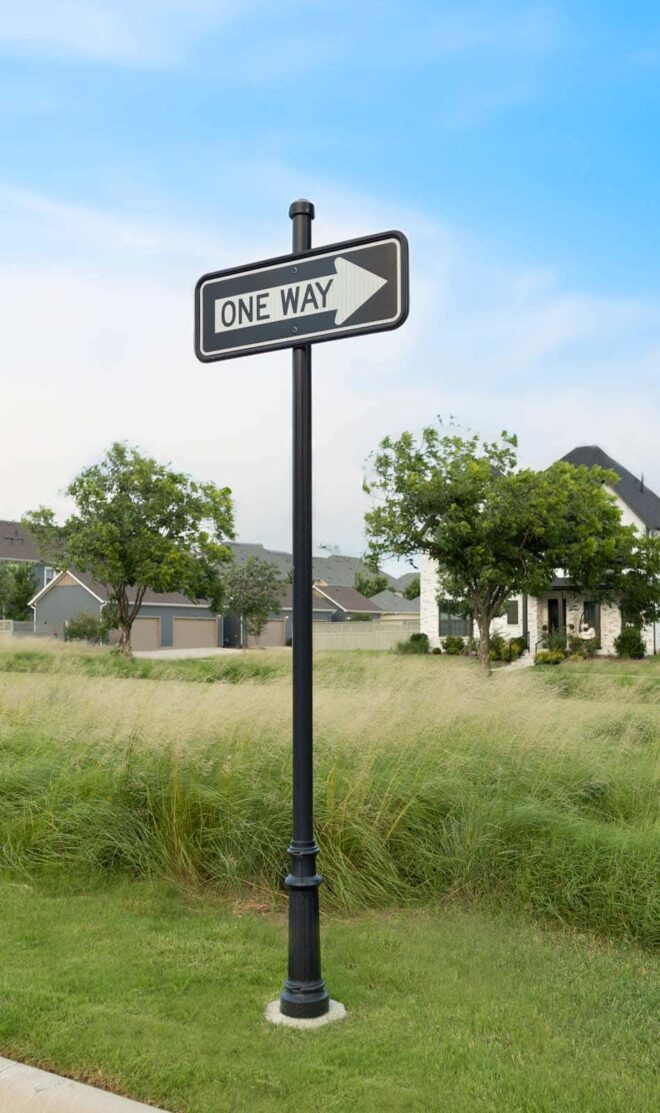 One way street sign on a round pole in a residential area.