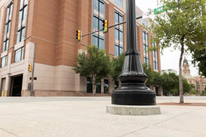 Ground-level view of a fluted lamp post with a decorative base on a city street.
