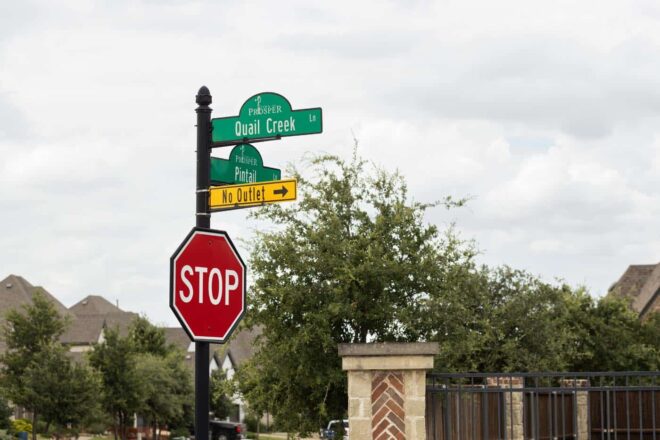Round pole and decorative finial top, with street signs, stop sign, and a no outlet sign in a residential neighborhood.