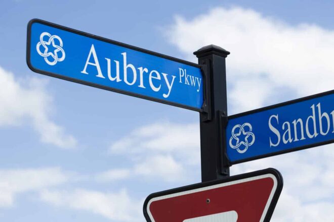 Close-up of a yield sign and street signs on a square pole with a square finial top.