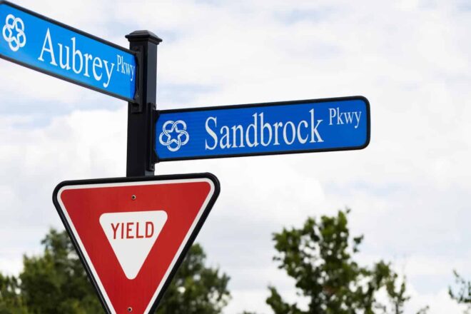 Close-up of a yield sign and street signs on a square pole with a square finial top.