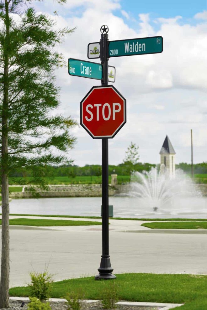 Street sign/Stop sign combo with a decorative star finial top in front of a fountain.