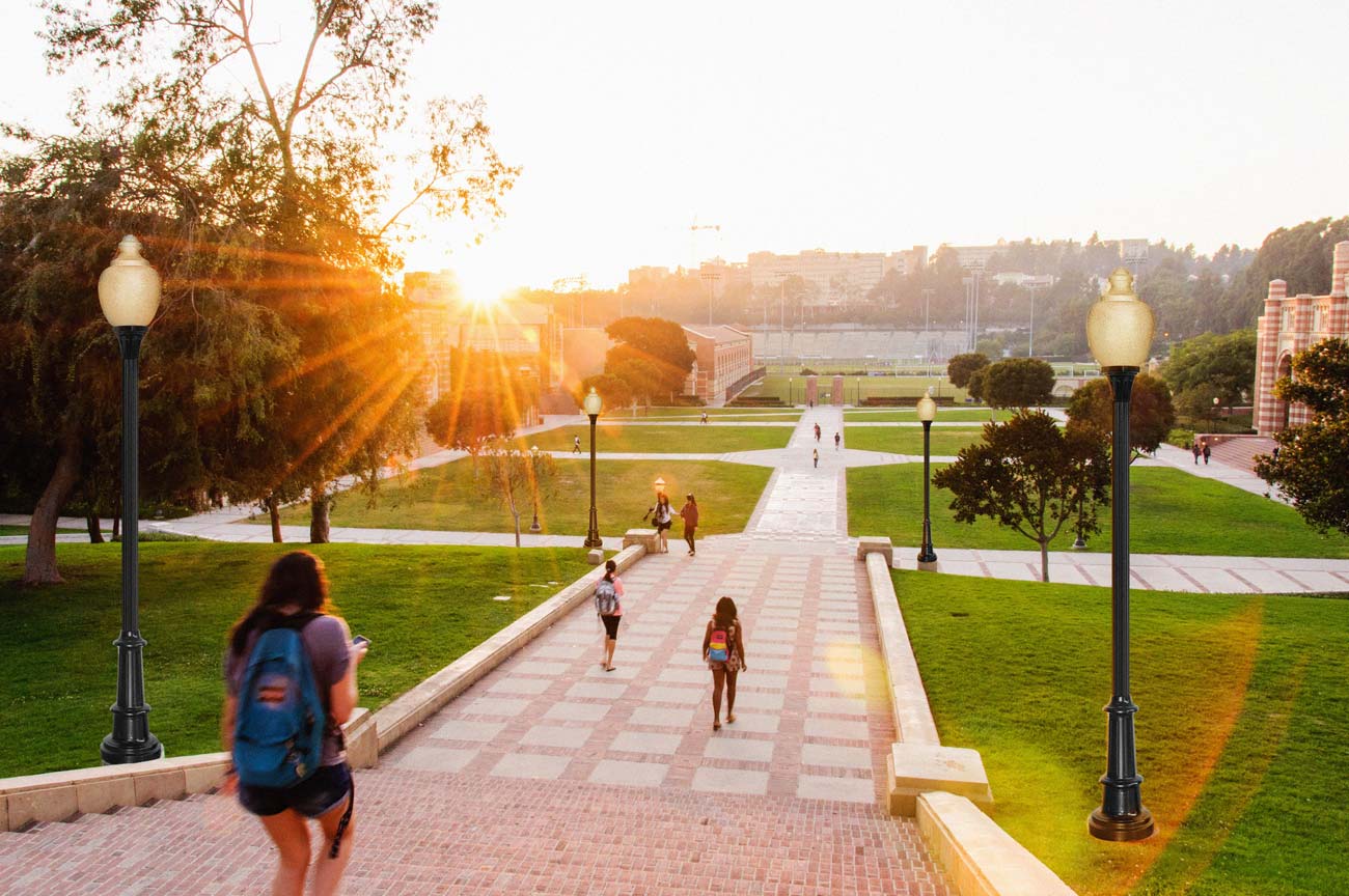 Students walking on an academic campus pathway lined by streetlamps