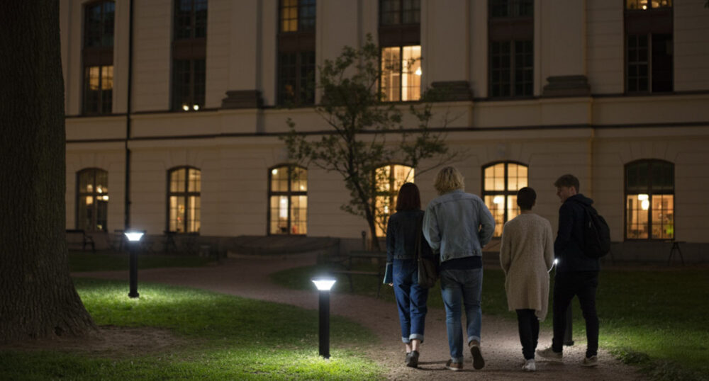 Four people walk along a path at night lit by pedestrian-scale bollards